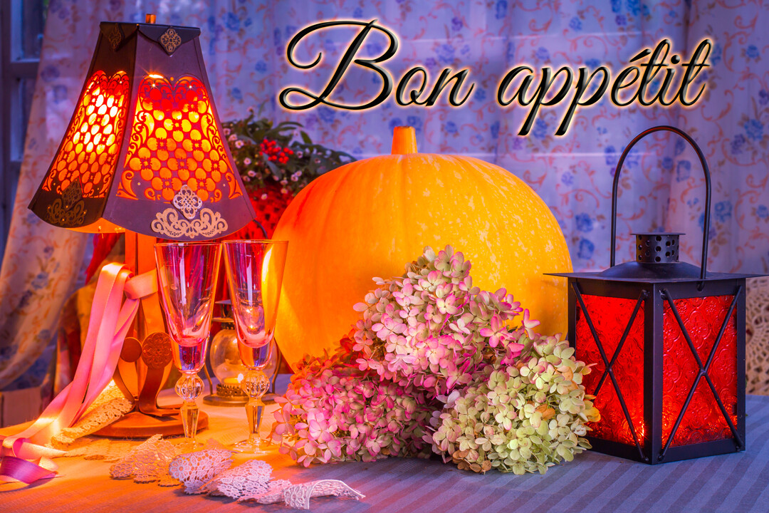 Une table dressée pour Halloween avec une citrouille, des lampes, des verres et des fleurs, dans une lumière chaude et tamisée.