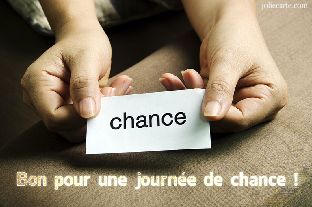 Deux mains humaines tiennent délicatement un petit papier blanc rectangulaire où le mot 'chance' est imprimé en noir, sur un fond marron texturé.